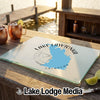 A rectangular glass cutting board featuring a map of Lake Lawtonka, Oklahoma, resting on an outdoor wooden table.