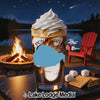 Dessert drink with whipped cream beside s'mores ingredients near a campfire at night.