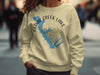 Cream sweatshirt with blue Cedar Creek Lake map and compass graphic and "TEXAS" text.