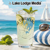 Glass with drink, limes, mint, and sunglasses on striped cushion at beach.