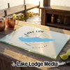 A glass cutting board featuring a blue map of Lake Erie rests on a wooden dock with drinks.