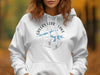 White hoodie with "Greers Ferry Lake Arkansas" graphic in blue over a compass rose.