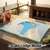 A glass cutting board printed with a blue map of Lake Stevens, Washington, rests on an outdoor wooden table near copper mugs and lime wedges.