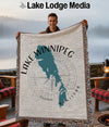 Man holds up a woven blanket featuring a teal outline of Lake Winnipeg, Manitoba.