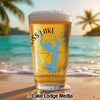 Glass of beer with "OSS LAKE" and compass design on a beach.