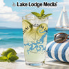 Glass with lime, mint, and ice on a beach with sunglasses and a sailboat.