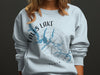Light blue sweatshirt with Falls Lake, North Carolina map and compass graphic.