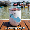 A white insulated tumbler with a Pearl Lake Wisconsin graphic sits on a wooden surface near water.