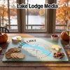 A glass cutting board featuring a blue map of Bass Lake, California, surrounded by cheese, crackers, and pecans.