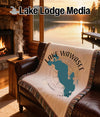 Lake Wawasee Indiana map blanket on a leather couch, with a fireplace and lake view.