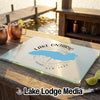 A rectangular glass cutting board featuring a blue map of Lake Ontario, compass rose, and text sits on a wooden outdoor bar.