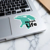 Turquoise sticker shaped like Lake Huron with "Huron Life" text on a laptop.