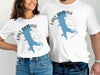 White t-shirts featuring a blue silhouette of Lake Quivira, Kansas, with a compass rose.