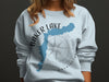Light blue sweatshirt with "Baker Lake Washington" text overlaying a blue map outline and compass rose.