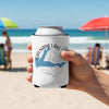 White koozie with Grenada Lake map and compass on a beach.