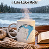 White mug with "Rushford Lake New York" and compass design beside a book.