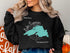 Black sweatshirt with teal Lake Superior map and compass graphic.