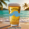Glass of beer with "Lake Superior" text and map on a beach at sunset.