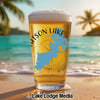 Beer glass with Watson Lake map and compass on beach with ocean background.