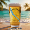 Glass of beer with "Skaneateles Lake" text and compass graphic on a beach.