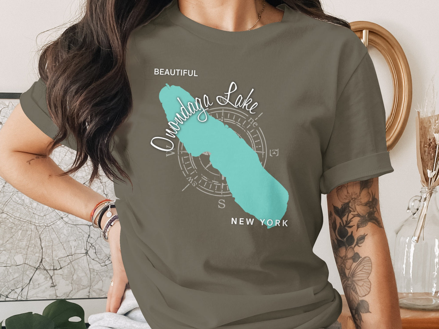 T-shirt featuring a turquoise silhouette of Onondaga Lake with compass rose and text.
