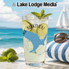 Glass with drink, lime, and mint on beach with sailboat and sunglasses.