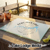 Glass cutting board featuring a Fort Peck Lake Montana map and compass design on a wooden table.