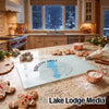 A glass cutting board featuring a blue lake silhouette and the text Barlow Lake Michigan rests on a kitchen counter amidst holiday baking supplies.