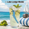 Tall glass of drink with lime and mint garnish on a beach.