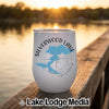 A white insulated wine tumbler featuring a blue map graphic and Silverwood Lake California text rests on a wooden dock with a lake sunset background.