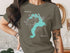 Woman wearing a grey t-shirt with "Lake Pond Orville Idaho" map graphic.