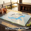 A rectangular glass cutting board rests on a wooden table, featuring a blue map of Lake Jackson, Georgia, over a compass design.