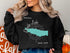 Black sweatshirt with a teal outline of Oneida Lake and a compass rose.