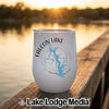 A white stemless wine tumbler rests on a wooden dock with a lake sunset in the background.