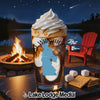 Glass of iced beverage with whipped cream, campfire, lake, and s'mores ingredients.