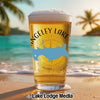 Beer glass with "Rangeley Lake" text and Maine outline on a beach.