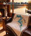Woven blanket with Evergreen Lake map design and compass rose, placed on a leather couch.