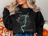 Black sweatshirt with "Beautiful Lake Okanagan British Columbia" text and compass design.