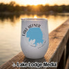 A white travel tumbler printed with a blue map outline of Lake Hefner, Oklahoma, resting on a wooden dock at sunset.