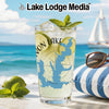 Glass with drink, lime, mint, sunglasses, and sailboat on a beach backdrop.