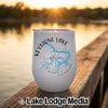 A white stemless wine tumbler with a Keystone Lake Oklahoma map design sits on a wooden dock at sunset.