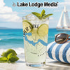 Glass of lemonade with lime, mint, and ice on a beach with a sailboat and sunglasses.
