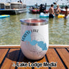 A white insulated wine tumbler featuring a Forest Lake, Minnesota compass design sits on a wooden boat deck with swimmers and boats in the background.