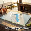 A rectangular glass cutting board rests on a wooden outdoor bar, featuring a blue map of Hudson Lake, Oklahoma, and compass graphics.