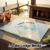 A textured glass cutting board printed with a Lake James North Carolina map and compass design sits on a wooden outdoor bar.