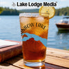 Glass of iced tea with lemon and "RAINBOW LAKE" text on a rustic table by a lake.