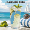 Glass with drink, lime, mint, and sunglasses on a beach with sailing boat.