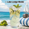 Glass with drink, lime, mint, and sunglasses on a beach with a sailboat.