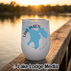 A white wine tumbler with a blue map of Lake Huron sits on a wooden dock at sunset.
