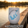 A white insulated wine tumbler sits on a wooden dock with a lake sunset in the background.